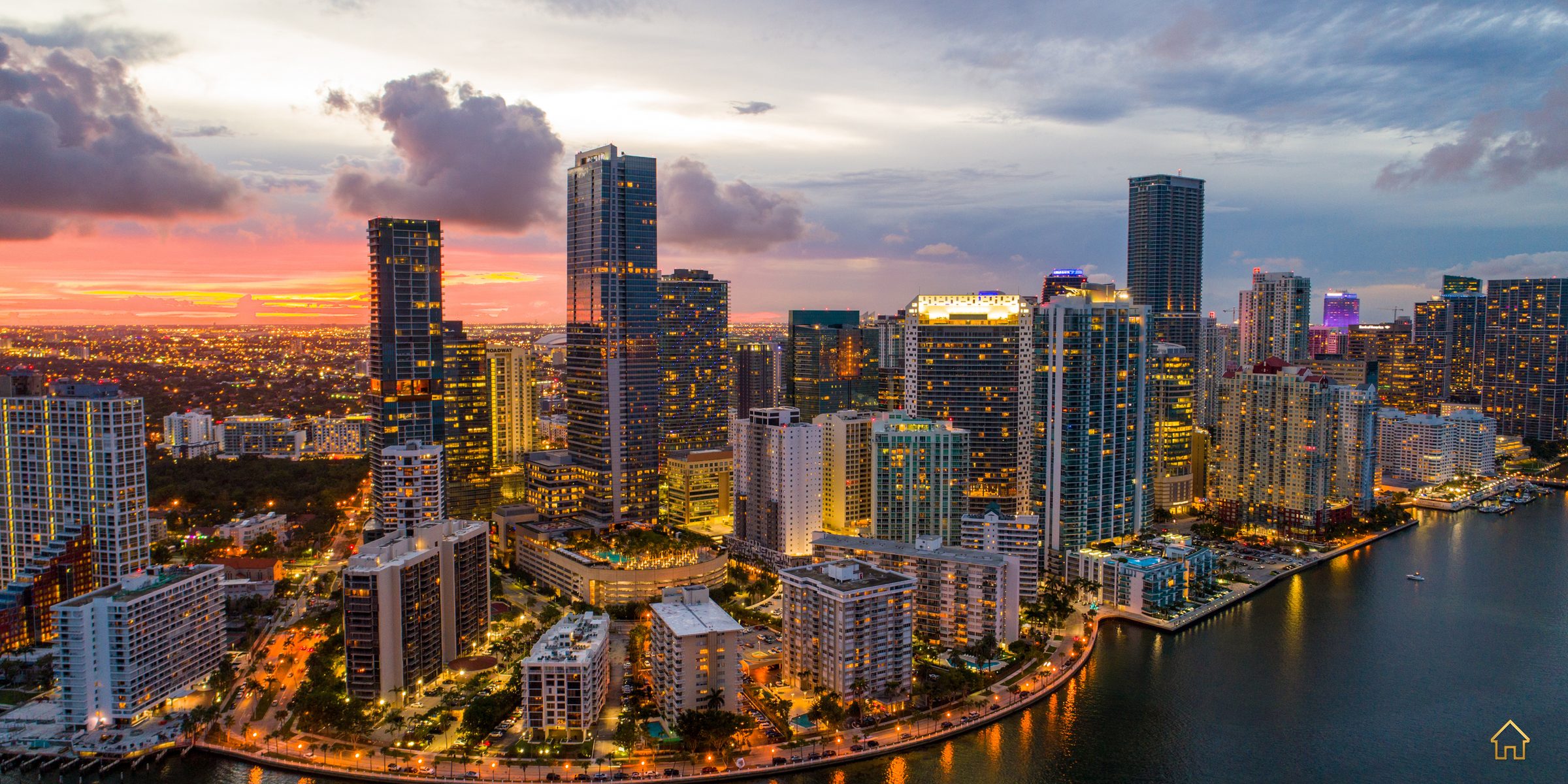 Aerial twilight view of the Brickell skyline and waterfront, towers lit against a sunset sky